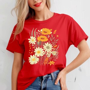 May include: A red t-shirt featuring a floral design with yellow and white daisies and sunflowers. The graphic includes green leaves and stems. The shirt is made of a soft material and is suitable for casual wear.
