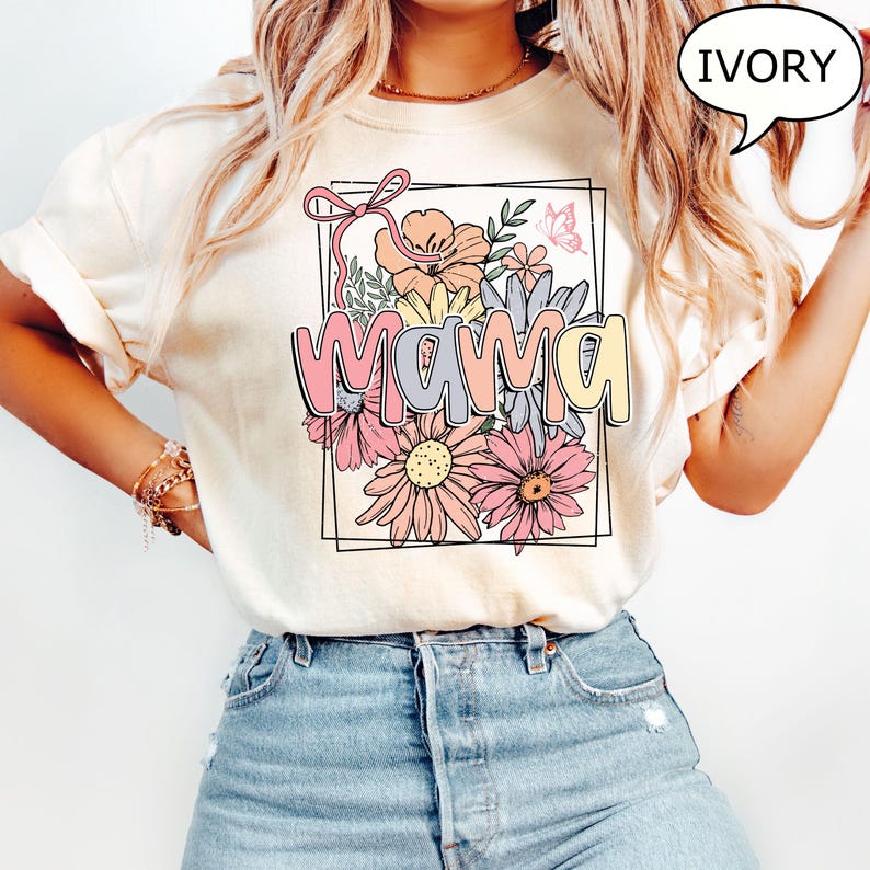 May include: A white t-shirt with a floral design and the word "mama" in a colorful font. The shirt is ivory in color.