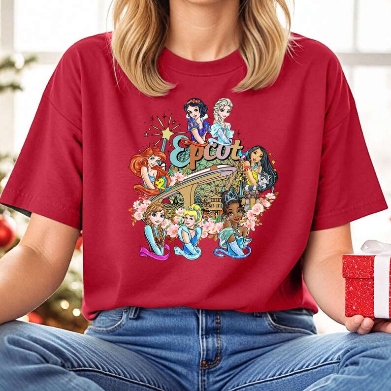 May include: Red t-shirt featuring a graphic of Disney princesses in front of the Epcot logo. The princesses include Snow White, Cinderella, Ariel, Belle, Tiana, and Mulan.