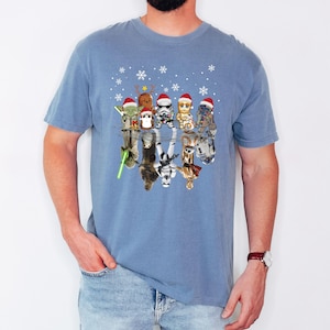 Puede incluir: Una camiseta azul con un dise&ntilde;o de Star Wars con tem&aacute;tica navide&ntilde;a. El dise&ntilde;o presenta varios personajes de Star Wars con gorros de Pap&aacute; Noel y reflejados en un charco de agua. Los personajes incluyen a Yoda, Chewbacca, Darth Vader, un Stormtrooper, R2-D2 y C-3PO.