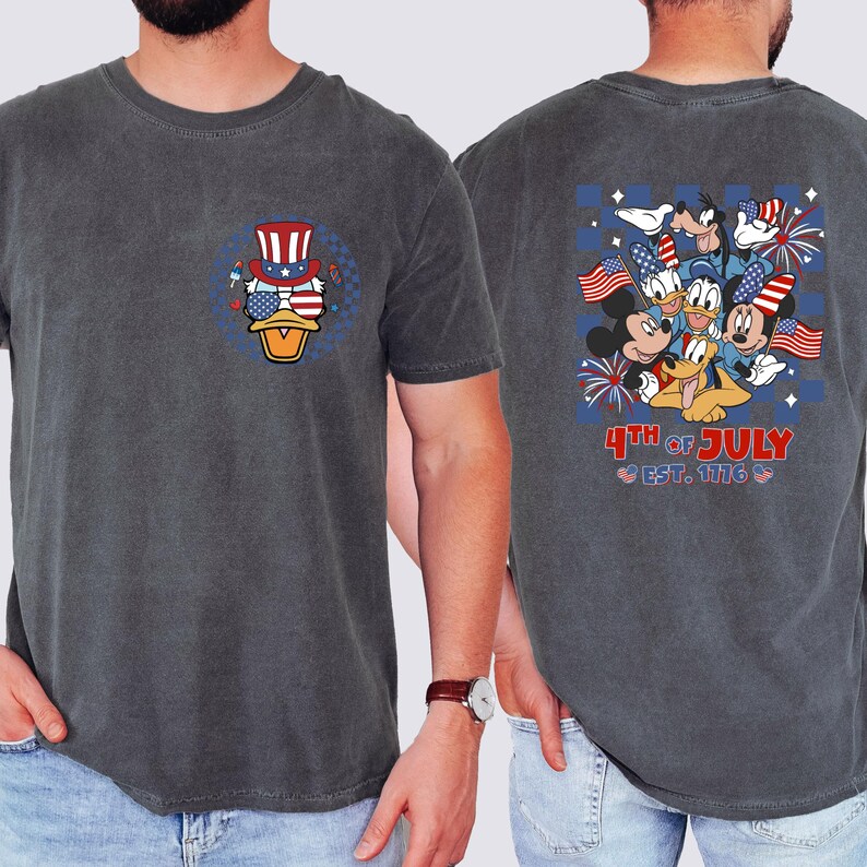 Pode incluir: Camiseta cinza escuro com um design patri&oacute;tico. A frente mostra um pato de desenho animado usando uma cartola e &oacute;culos de sol com um design de bandeira americana. A parte de tr&aacute;s da camisa mostra Mickey, Donald, Pateta e Pluto celebrando o 4 de julho.