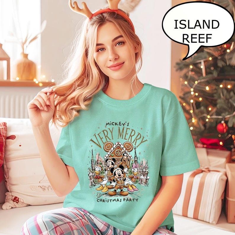 Pu&ograve; includere: Maglietta verde acqua con la scritta "Mickey's Very Merry Christmas Party" e una grafica di Topolino, Minnie, Paperino e Pippo davanti a una casa di pan di zenzero. Articolo a tema natalizio.