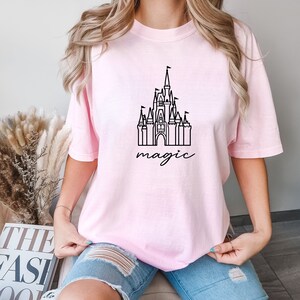May include: A pink t-shirt with a black outline of Cinderella's castle and the word "magic" underneath.