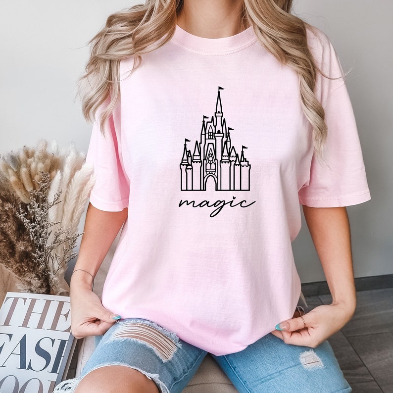 May include: A pink t-shirt with a black outline of Cinderella's castle and the word "magic" underneath.