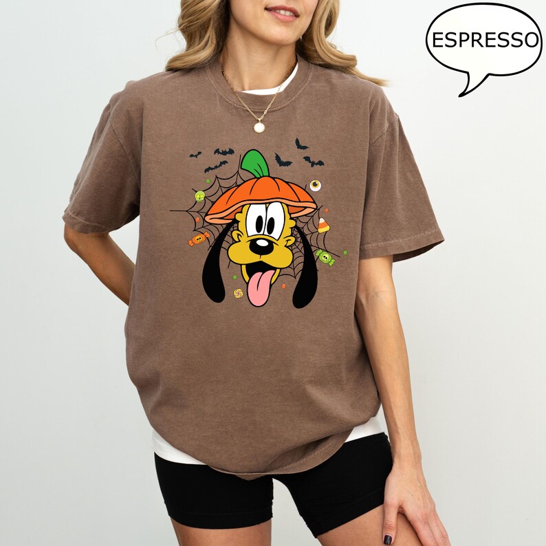 Może przedstawiać: Brązowa koszulka z Plutonem w kapeluszu z dyni, z pajęczyną, nietoperzami i cukierkami. Słowo "ESPRESSO" znajduje się w dymku. Koszulka ma wygodny kr&oacute;j.