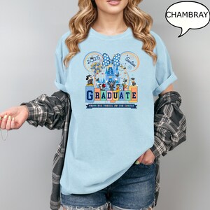 以下が含まれることがあります： 薄い青色のTシャツに、ミッキーマウスの耳、城、そして「Graduate from the tassel to the castle」という文字が描かれたグラフィックがプリントされています。グラフィックには、「2025」と「Senior」という文字も含まれています。