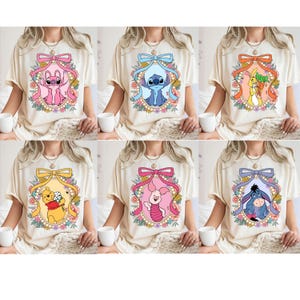 May include: Six different t-shirts with a cartoon character in a floral frame. The characters are Stitch, Winnie the Pooh, Piglet, Eeyore, and two others. The shirts are all a light beige color.