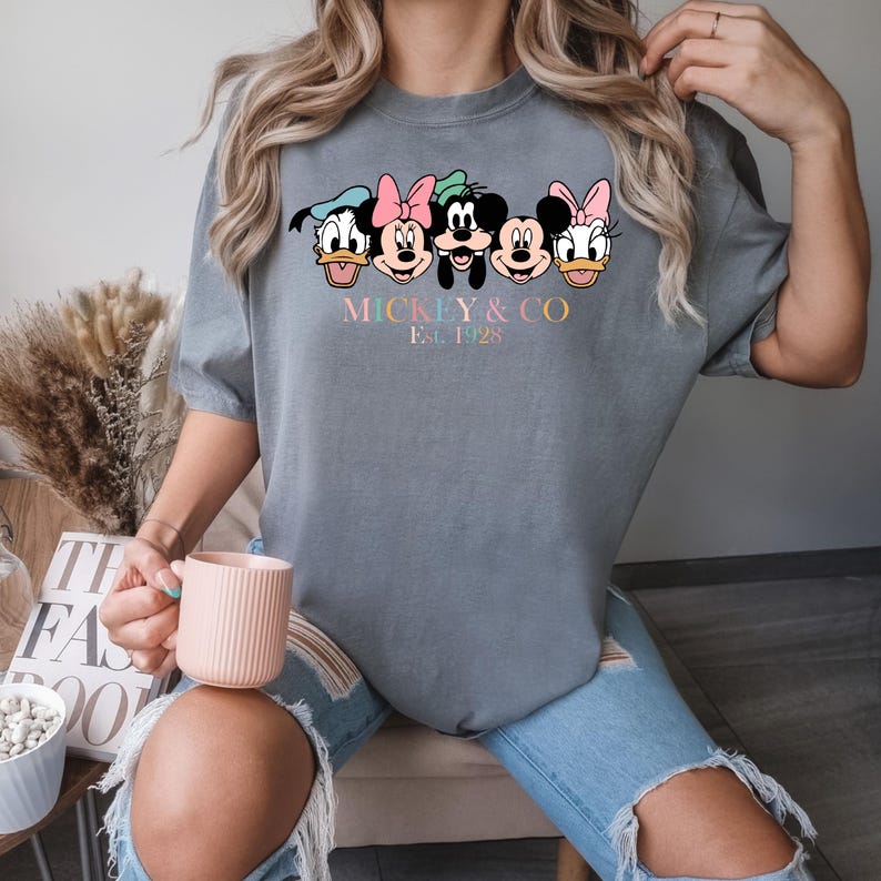 May include: A gray t-shirt with a graphic of Mickey Mouse and his friends. The text "Mickey & Co. Est. 1928" is printed below the graphic.