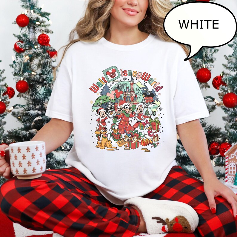 May include: White t-shirt with a colorful graphic featuring Disney characters in a Christmas theme. The text "Walt Disney World" is displayed above the characters. The shirt is part of a holiday collection.