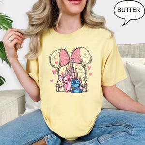 Puede incluir: Camiseta amarilla con un gr&aacute;fico de un lazo rosa, un castillo y personajes de dibujos animados. El dise&ntilde;o incluye corazones rosas y la palabra "BUTTER" en un bocadillo. La camiseta la lleva una persona.