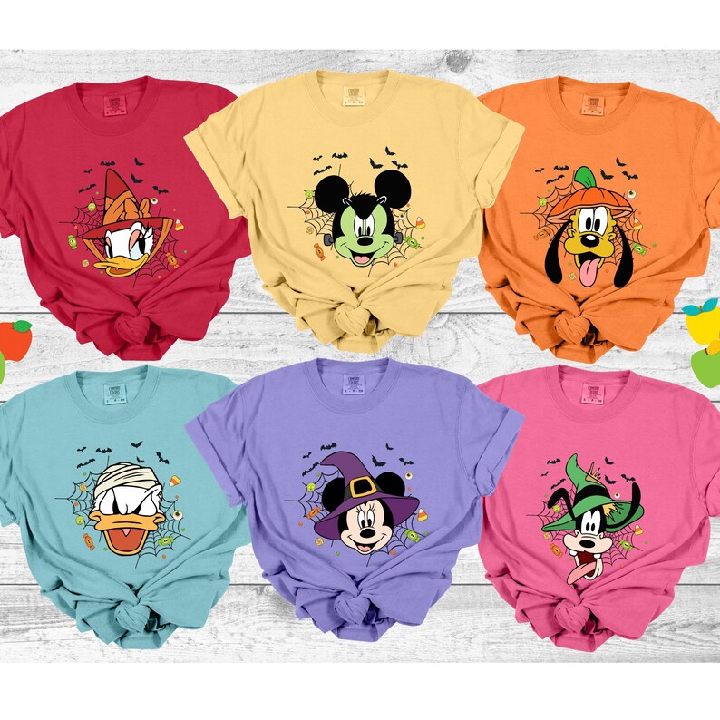 Może przedstawiać: Sześć kolorowych koszulek z postaciami Disneya w kostiumach na Halloween. Koszulki są czerwone, ż&oacute;łte, pomarańczowe, niebieskie, fioletowe i r&oacute;żowe. Każda koszulka ma inną postać, w tym Kaczora Donalda, Myszki Miki i Psa Pluto, z pajęczynami i nietoperzami.