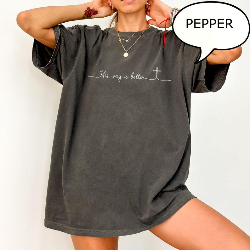 May include: Dark gray t-shirt with the text "His way is better" and a cross graphic. The shirt has a relaxed fit and short sleeves. The word "PEPPER" is in a speech bubble.