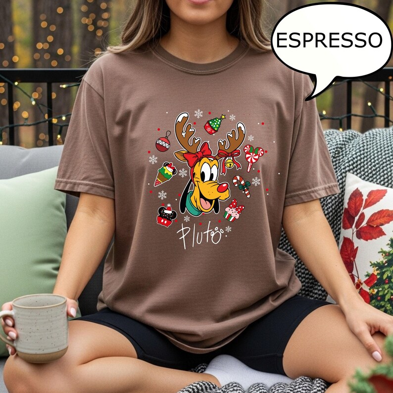 May include: A brown t-shirt with a graphic of Pluto wearing reindeer antlers and Christmas decorations. The word "Pluto" is written below the graphic in a cursive font. The word "ESPRESSO" is in a speech bubble.
