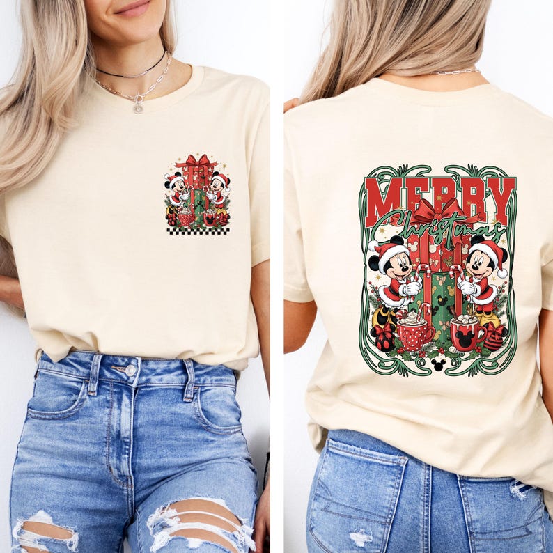 May include: A cream-coloured t-shirt with a Christmas design. The front shows Mickey and Minnie Mouse with gifts. The back of the shirt has the words "MERRY Christmas" with Mickey and Minnie Mouse. The design includes red, green, and black accents.