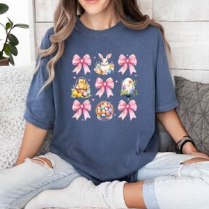 Puede incluir: Una camiseta azul marino con un dise&ntilde;o gr&aacute;fico que presenta lazos rosas, un conejito, un pollito y huevos de Pascua. El dise&ntilde;o se repite nueve veces en la camiseta.