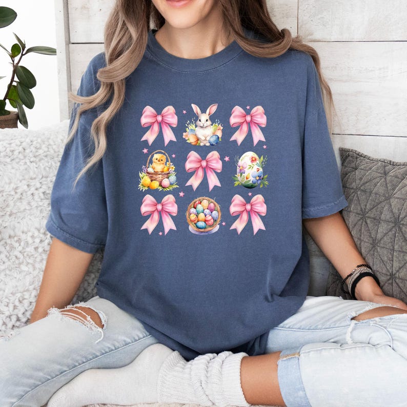 Puede incluir: Una camiseta azul marino con un dise&ntilde;o gr&aacute;fico que presenta lazos rosas, un conejito, un pollito y huevos de Pascua. El dise&ntilde;o se repite nueve veces en la camiseta.