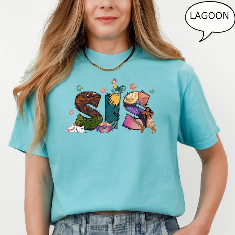May include: A turquoise blue t-shirt featuring a graphic of the word "SIS" made up of images from the Disney film Moana. The letters are decorated with flowers, a rooster, a crab, and a character from the film.