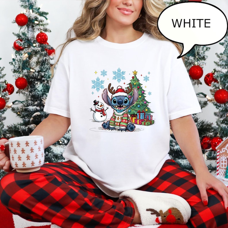 Puede incluir: Camiseta blanca de cuello redondo con un personaje de dibujos animados que lleva un jersey navide&ntilde;o, cuernos y un gorro de Pap&aacute; Noel. Tambi&eacute;n se representa un &aacute;rbol de Navidad, un mu&ntilde;eco de nieve y copos de nieve. La palabra "WHITE" est&aacute; en un bocadillo.