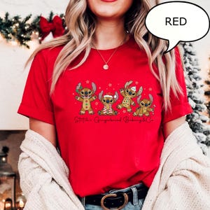 Puede incluir: Una camiseta roja con un gr&aacute;fico de cuatro personajes Stitch con tem&aacute;tica de pan de jengibre, cada uno con decoraciones festivas. El texto "Stitch's Gingerbread Baking & Co." est&aacute; impreso debajo. Es visible un bocadillo con la palabra "RED".