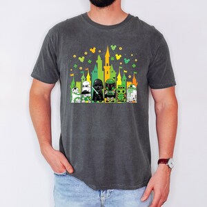 Puede incluir: Camiseta gris oscuro con un gr&aacute;fico colorido de personajes de Star Wars frente a un castillo. El dise&ntilde;o incluye elementos verdes, amarillos y blancos, con tr&eacute;boles y orejas de Mickey Mouse. La camiseta es c&oacute;moda e informal.