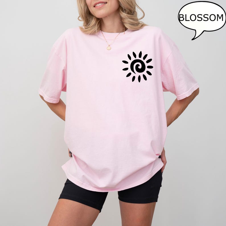 May include: A pink oversized t-shirt with a black sun graphic and the word "BLOSSOM" in a speech bubble.
