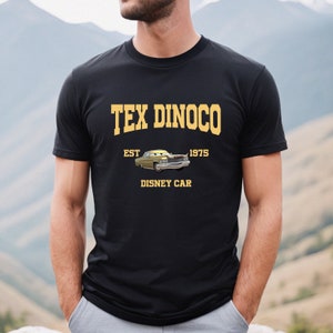 Puede incluir: Una camiseta negra con un dise&ntilde;o gr&aacute;fico amarillo que presenta el texto "Tex Dinoco Est. 1975" y una imagen de dibujos animados de un coche amarillo. El texto "Disney Car" tambi&eacute;n est&aacute; incluido en el dise&ntilde;o.