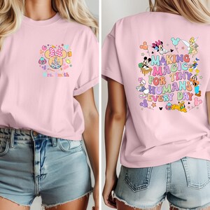 May include: Pale pink t-shirt with a Minnie Mouse design and the text "Mrs. Smith" on the front. The back of the shirt has a colourful graphic with Disney characters and the words "Making Magic for Tiny Humans Every Day."