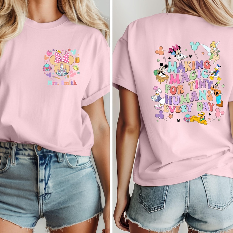 May include: Pale pink t-shirt with a Minnie Mouse design and the text "Mrs. Smith" on the front. The back of the shirt has a colourful graphic with Disney characters and the words "Making Magic for Tiny Humans Every Day."