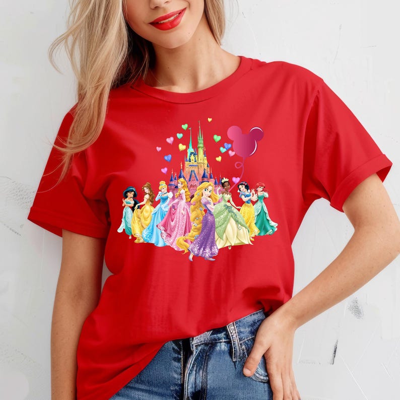 May include: Red t-shirt with a graphic of Disney princesses in front of Cinderella's castle with a Mickey Mouse balloon and hearts.