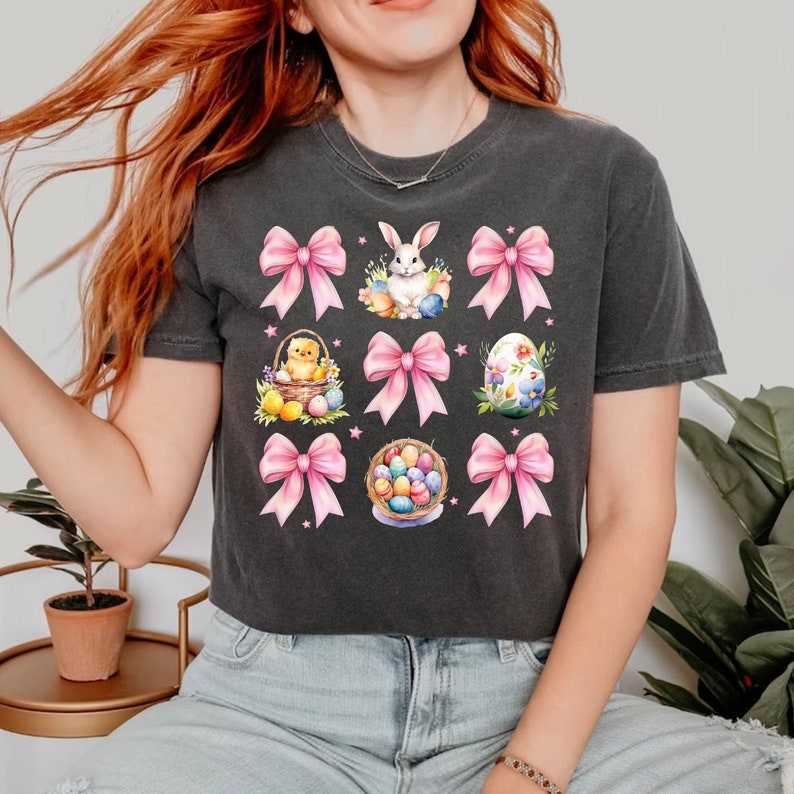 Puede incluir: Una camiseta negra recortada con un dise&ntilde;o de Pascua rosa y blanco. El dise&ntilde;o incluye un conejito, pollitos, huevos y lazos.