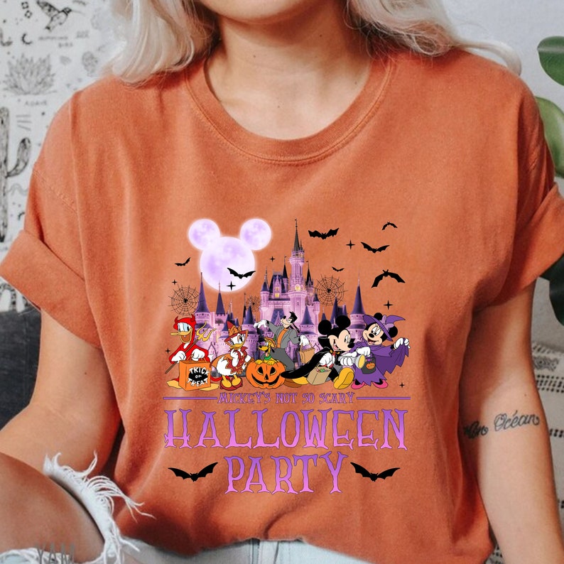 May include: Orange t-shirt with a Halloween party design featuring Mickey Mouse and other Disney characters in front of Cinderella's Castle. The text reads "Ain't's Not So Scary - Halloween Party".