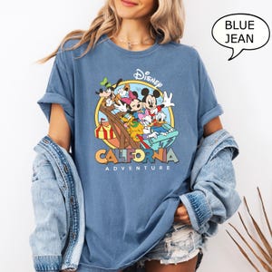 Puede incluir: Una camiseta azul con un gr&aacute;fico de Mickey Mouse y sus amigos montando una monta&ntilde;a rusa en Disney California Adventure. El texto "Disney California Adventure" est&aacute; impreso debajo del gr&aacute;fico.