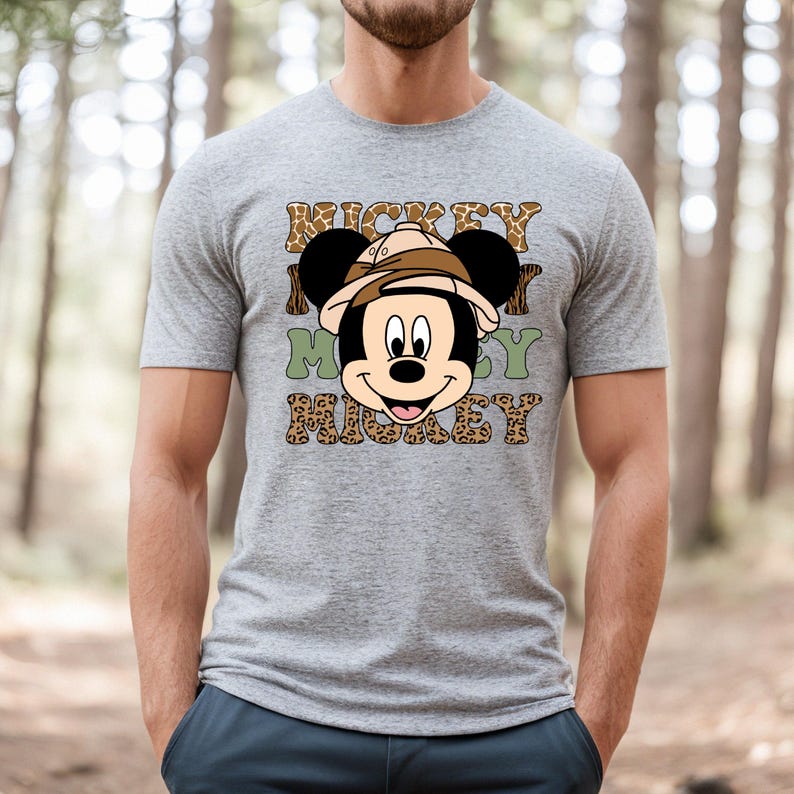 May include: A grey t-shirt featuring a cartoon image of Mickey Mouse wearing a safari hat. The text "Mickey Mickey Mickey" is printed on the shirt in a leopard print pattern.