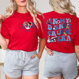 Op de afbeelding: Rood T-shirt met een Mickey Mouse-afbeelding aan de voorkant en de tekst "In My Disney Cruise Era" op de achterkant. Het shirt wordt gecombineerd met grijze shorts.