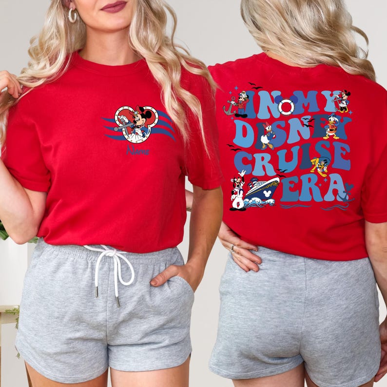 Op de afbeelding: Rood T-shirt met een Mickey Mouse-afbeelding aan de voorkant en de tekst "In My Disney Cruise Era" op de achterkant. Het shirt wordt gecombineerd met grijze shorts.