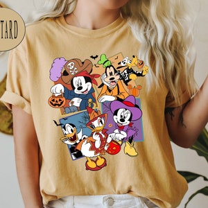 K&ouml;nnte beinhalten: Ein senfgelbes T-Shirt mit einem grafischen Druck von Mickey Mouse, Minnie Mouse, Donald Duck, Goofy und Pluto in Halloween-Kost&uuml;men. Die Figuren halten K&uuml;rbisse und S&uuml;&szlig;igkeiten.