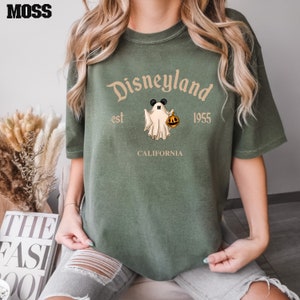 Puede incluir: Camiseta verde con un logotipo de Disneyland de estilo vintage que presenta un fantasma sosteniendo una calabaza. El texto dice "Disneyland est 1955 California".