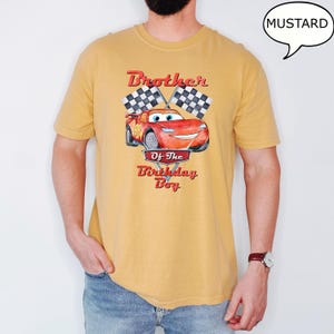 Puede incluir: Una camiseta amarilla mostaza con una imagen de dibujos animados de un coche de carreras rojo y banderas a cuadros. El texto "Brother of the Birthday Boy" est&aacute; impreso en la camiseta.