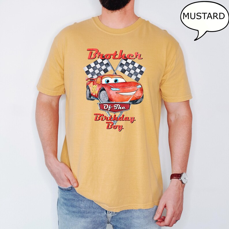 Puede incluir: Una camiseta amarilla mostaza con una imagen de dibujos animados de un coche de carreras rojo y banderas a cuadros. El texto "Brother of the Birthday Boy" est&aacute; impreso en la camiseta.