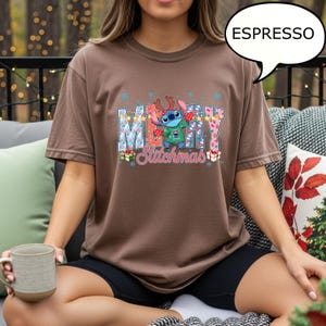 Op de afbeelding: Espresso-kleurige t-shirt met een feestelijke Stitch-afbeelding met de tekst "MERRY Stitchmas". Het ontwerp bevat sneeuwvlokken, geschenkdozen en Stitch met een rendiergeweige haarband. De shirt is een comfortabele, casual stijl.