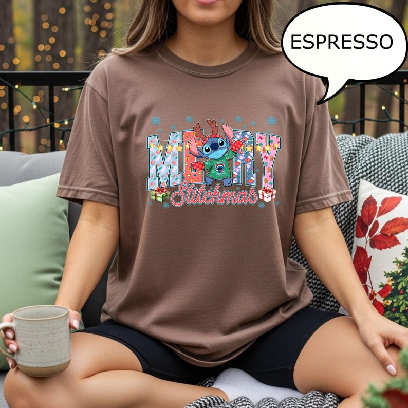 Op de afbeelding: Espresso-kleurige t-shirt met een feestelijke Stitch-afbeelding met de tekst "MERRY Stitchmas". Het ontwerp bevat sneeuwvlokken, geschenkdozen en Stitch met een rendiergeweige haarband. De shirt is een comfortabele, casual stijl.