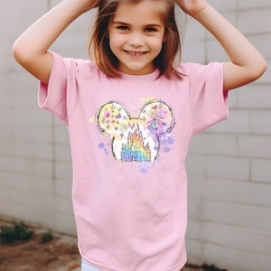 Puede incluir: Una camiseta rosa con un gr&aacute;fico colorido de una cabeza de Mickey Mouse con el castillo de Cenicienta en su interior. El castillo est&aacute; delineado en negro y tiene un efecto arco&iacute;ris. El fondo es un efecto de pintura salpicada blanca.