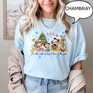 May include: Light blue t-shirt with a festive graphic featuring cartoon characters in Santa hats and a Christmas tree. The text "It's the most wonderful time of the year" is printed below the graphic.