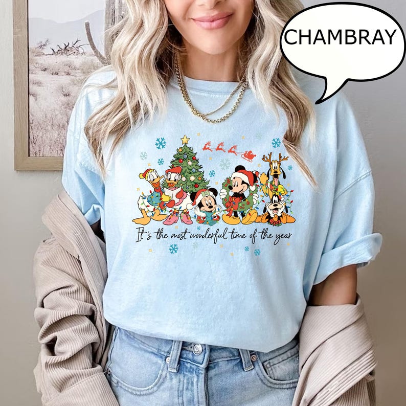 May include: Light blue t-shirt with a festive graphic featuring cartoon characters in Santa hats and a Christmas tree. The text "It's the most wonderful time of the year" is printed below the graphic.
