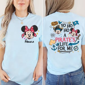 May include: Light blue t-shirt with a Mickey Mouse character on the front and a pirate themed design on the back. The back design includes the text "Yo Ho Ho A Pirate's Life For Me".