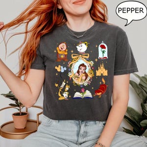 May include: A dark gray cropped t-shirt with a graphic print of various characters from the Disney movie Beauty and the Beast. The characters include Belle, Beast, Lumiere, Cogsworth, Mrs. Potts, Chip, and the enchanted rose. The text "PEPPER" is visible in a speech bubble in the upper right corner of the image.