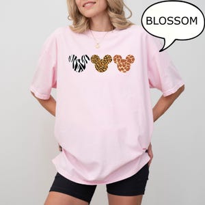 Pu&ograve; includere: T-shirt rosa chiaro con tre disegni a testa di Mickey Mouse con stampa animalier: zebra, leopardo e giraffa. La parola "BLOSSOM" &egrave; in una nuvoletta. La maglietta ha una vestibilit&agrave; ampia.