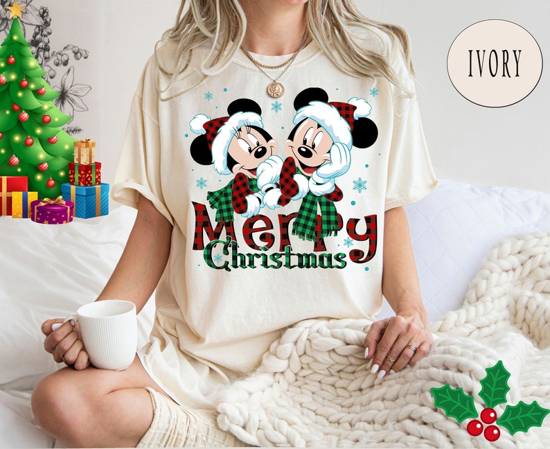 May include: A white t-shirt with a red and green plaid design featuring Mickey Mouse and Minnie Mouse wearing Santa hats and scarves. The text "Merry Christmas" is written in red and green plaid letters.