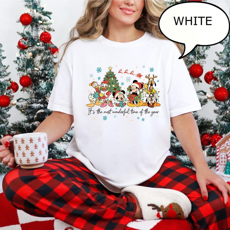 May include: White t-shirt featuring a festive graphic of Disney characters, including Mickey and Minnie Mouse, in holiday attire. The shirt has the text "It's the most wonderful time of the year". The person is wearing red and black plaid pajama pants.