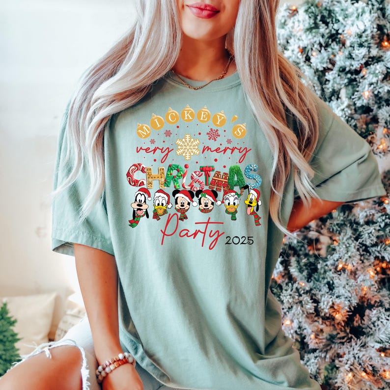 K&ouml;nnte beinhalten: Ein hellgr&uuml;nes T-Shirt mit einem Weihnachtsmotiv mit Mickey Mouse und seinen Freunden. Der Text auf dem Shirt lautet "Mickey's very merry Christmas Party 2025".